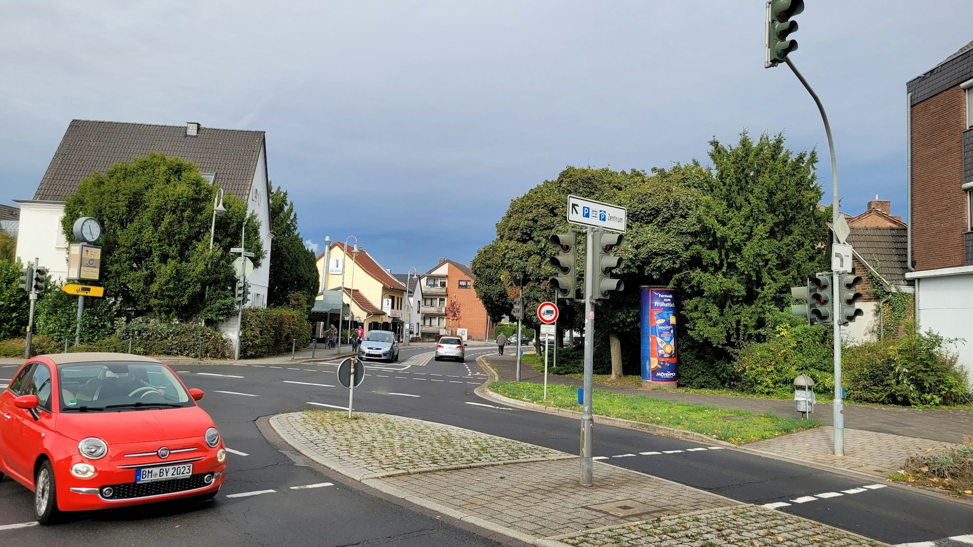 Eine Kreuzung, im Vordergrund eine Fußgängerinsel und ein Auto.