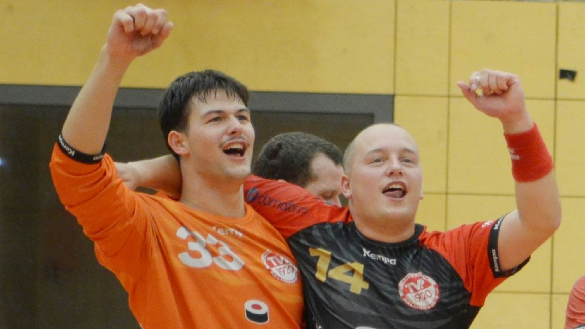 Die beiden Handballer jubeln, Arm in Arm, in Richtung Tribüne.