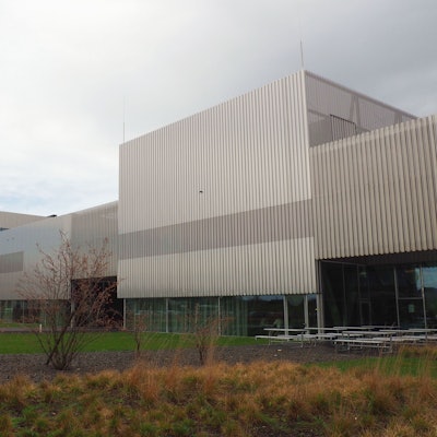 Ein großer Gebäudekomplex aus Beton und Glas steht an einer Grünanlage.