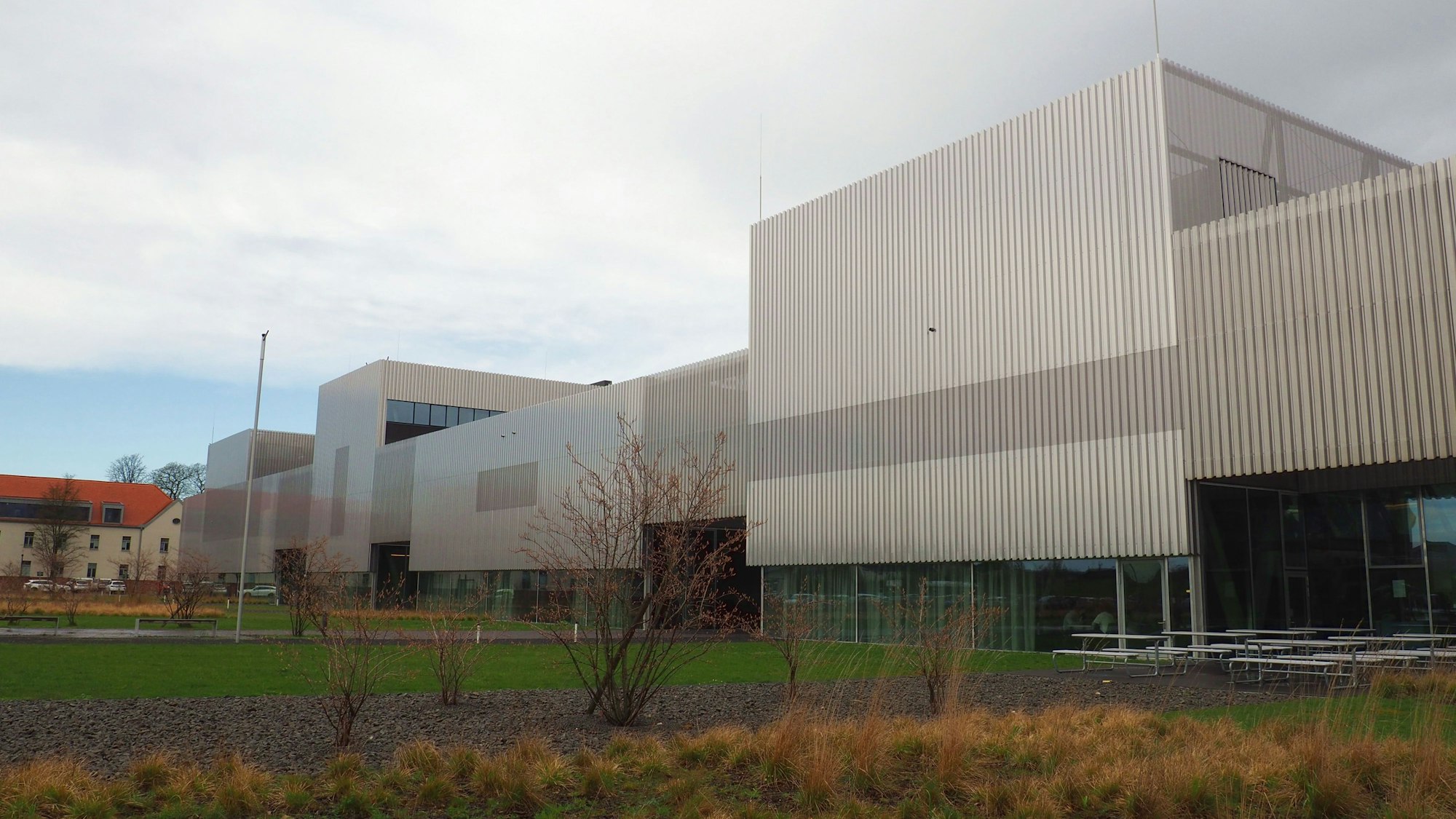 Ein großer Gebäudekomplex aus Beton und Glas steht an einer Grünanlage.