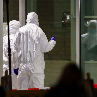 Polizeibeamte der Spurensicherung in weißen Schutzanzügen untersuchen Löcher in Glasscheiben des Kinos. Im Foyer eines großen Kinos am Hauptbahnhof in Krefeld hat die Polizei in der vergangenen Woche einen Brandstifter niedergeschossen.