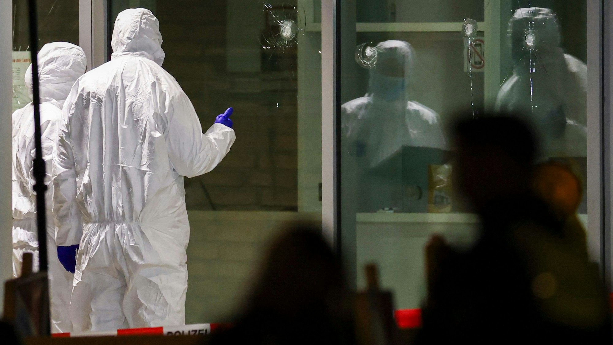 Polizeibeamte der Spurensicherung in weißen Schutzanzügen untersuchen Löcher in Glasscheiben des Kinos. Im Foyer eines großen Kinos am Hauptbahnhof in Krefeld hat die Polizei in der vergangenen Woche einen Brandstifter niedergeschossen.