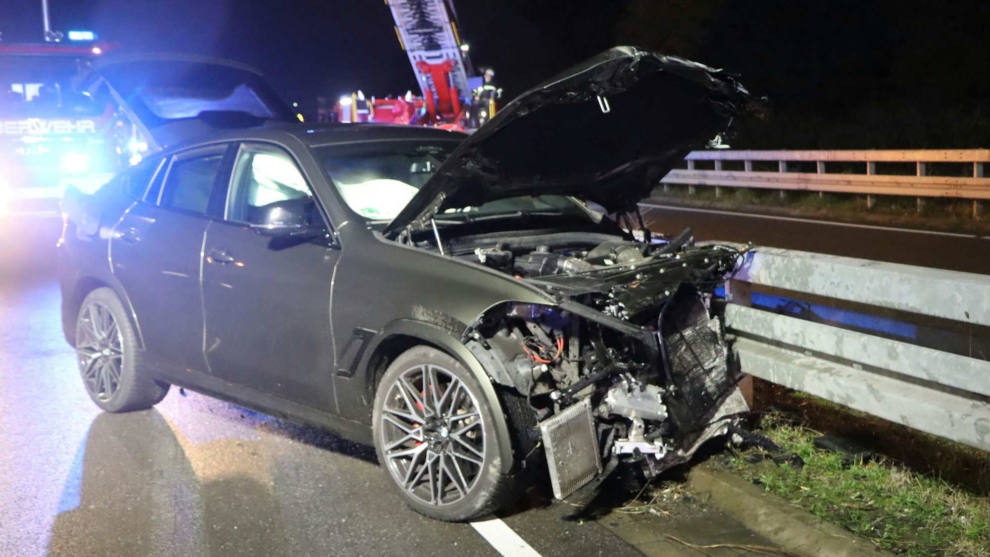 Ein Auto ist frontal in eine Leitplanke gefahren. Die Vorderseite des Fahrzeugs ist stark beschädigt, die Motorhaube eingedrückt.
