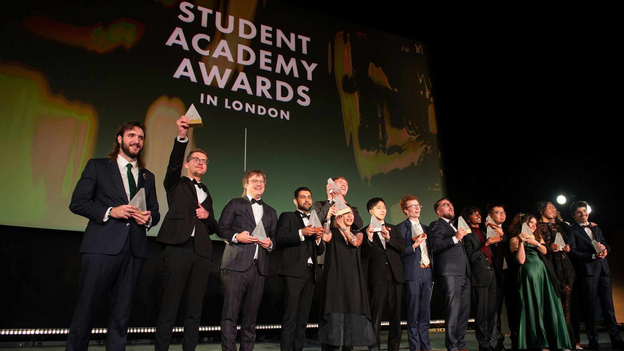 Junge Leute in Festkleidung jubeln auf einer Bühne.