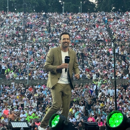 Ein Mann steht mit einem Mikro in der Hand auf einer Bühne.