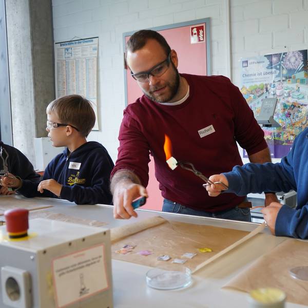 Das Bild zeigt einen Lehrer und einen Jungen bei einem chemischen Experiment mit Feuer.