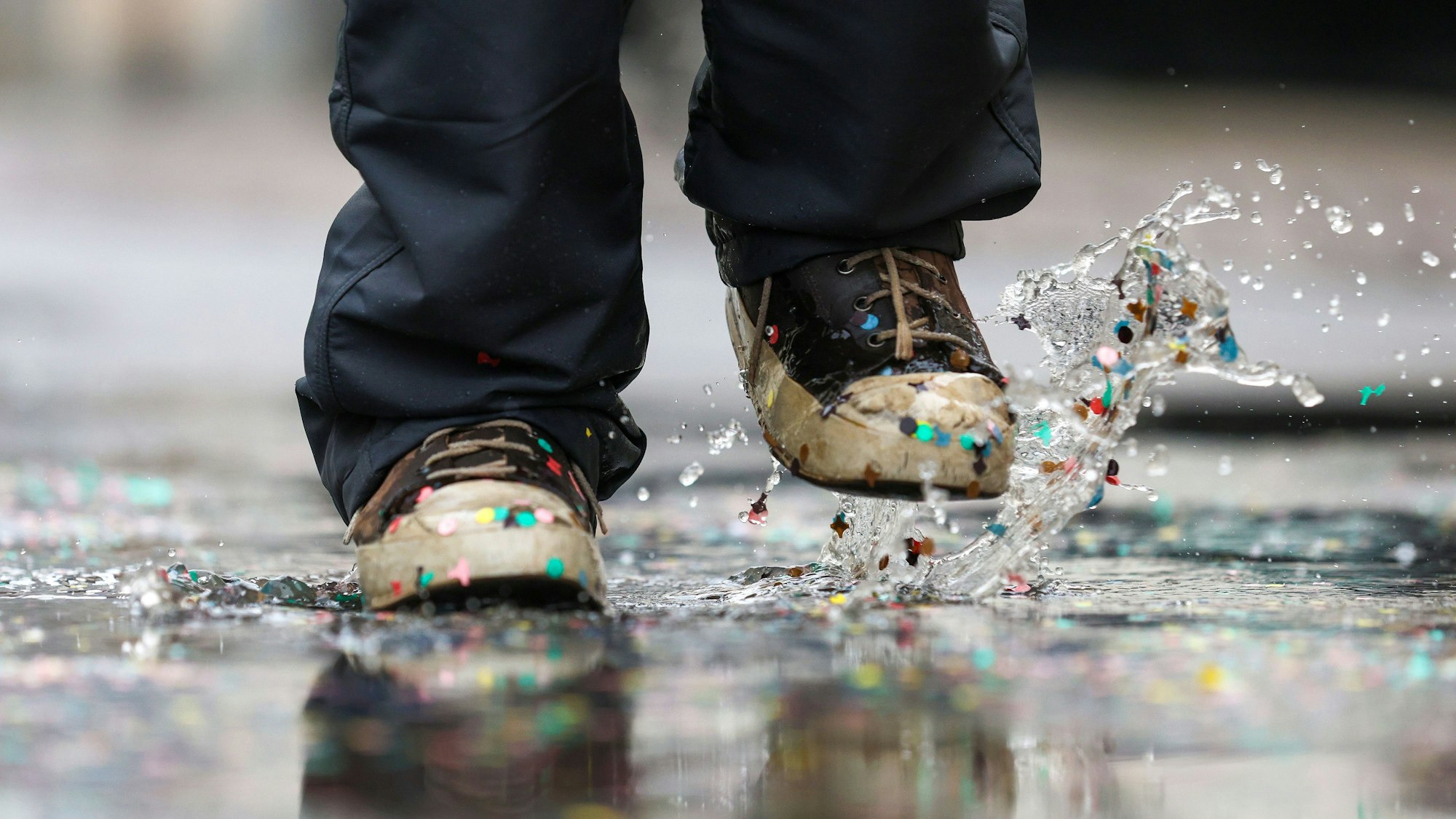 Ein Mann geht durch eine Pfütze, in der Konfetti liegt.
