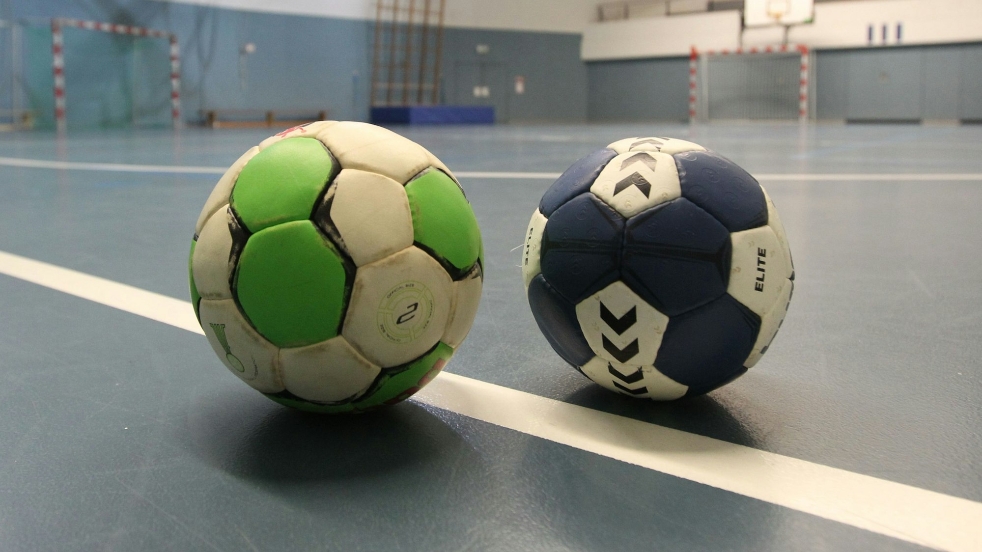 Zwei Handbälle liegen auf einem Turnhallenboden