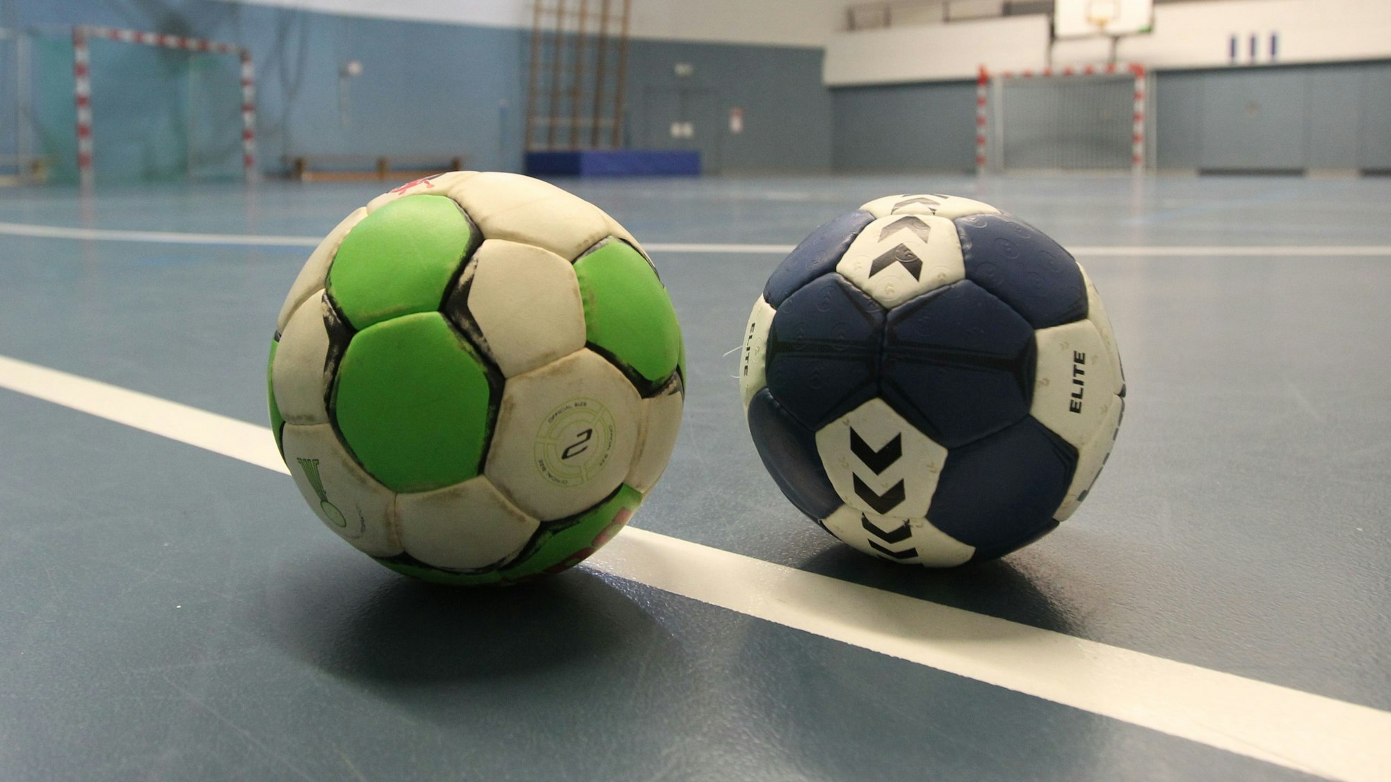 Zwei Handbälle liegen auf einem Turnhallenboden