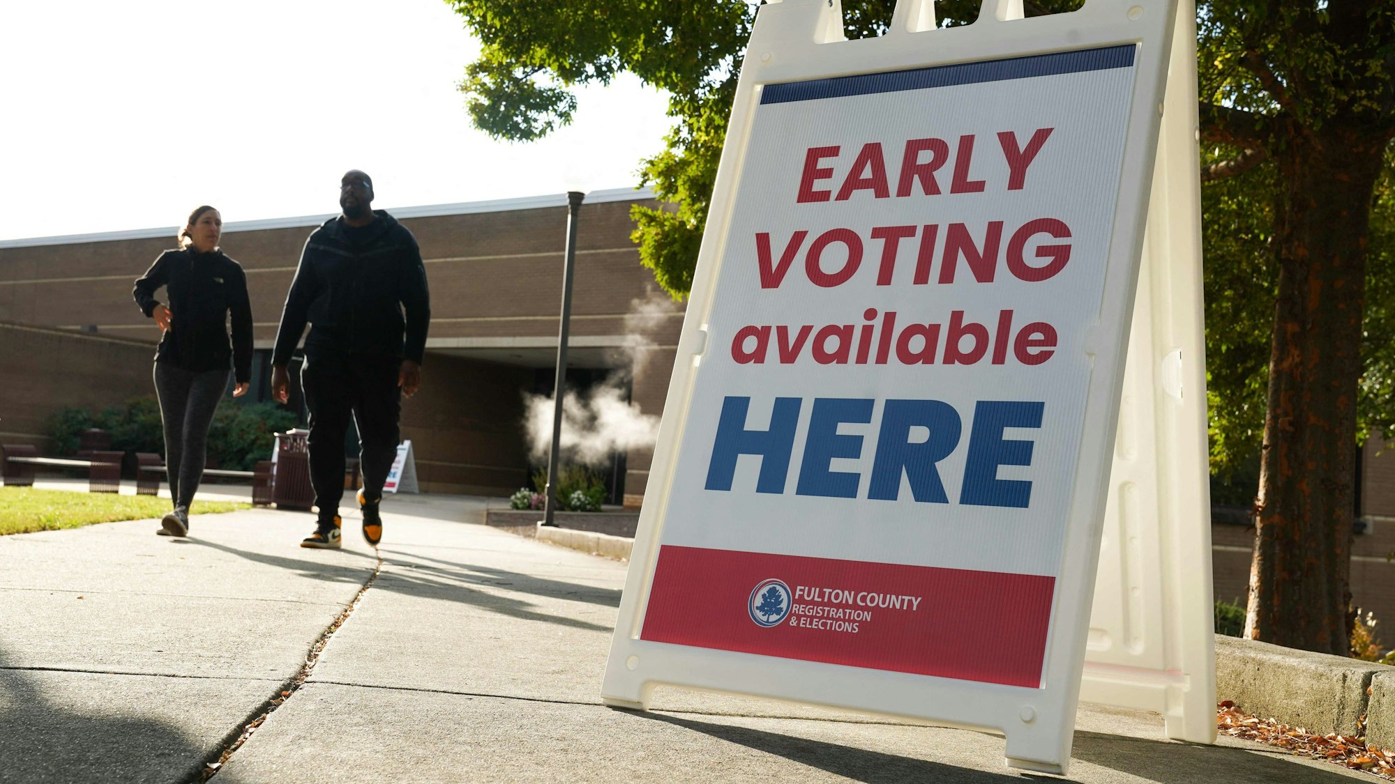Ein Schild mit der Aufschrift „Vote Early“ steht an einem Fußweg.