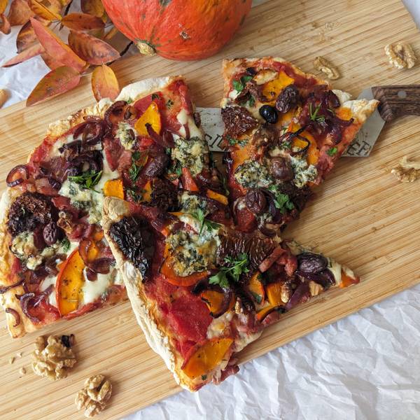 Eine in Stücke geschnittene Pizza liegt auf einem Holzbrett.