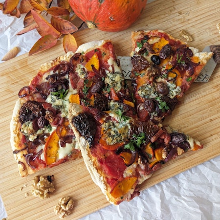 Eine in Stücke geschnittene Pizza liegt auf einem Holzbrett.