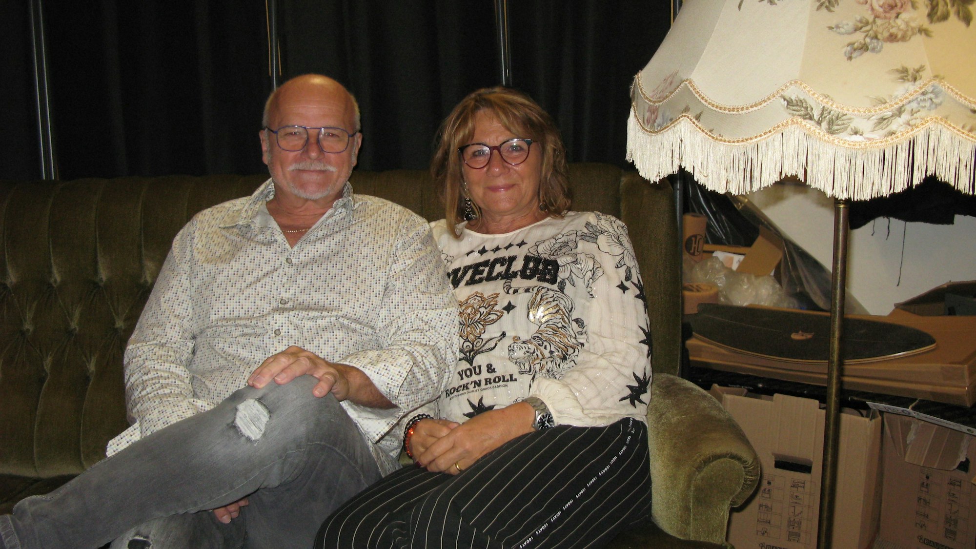 Ingo und Gaby Teusch sitzen auf dem Hennefer Sofa, rechts daneben steht eine altmodische Stehlampe.