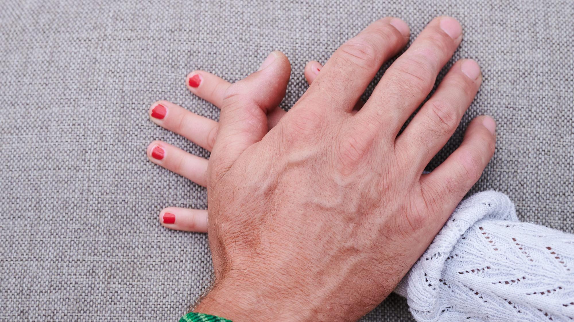 Eine Männerhand liegt auf einer Mädchenhand.