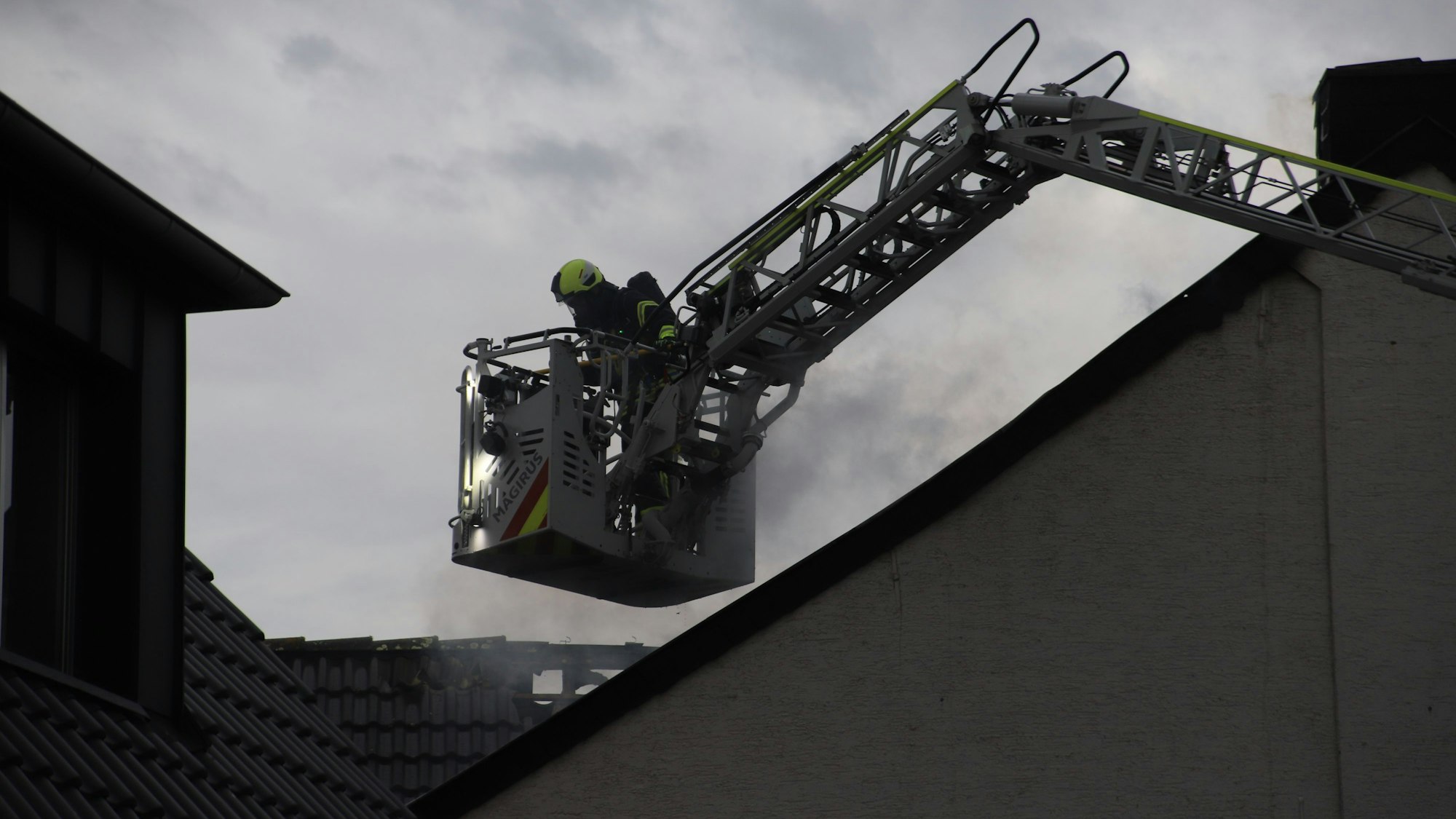 Ein Feuerwehrmann im Korb einer Drehleiter bekämpft einen Brand.