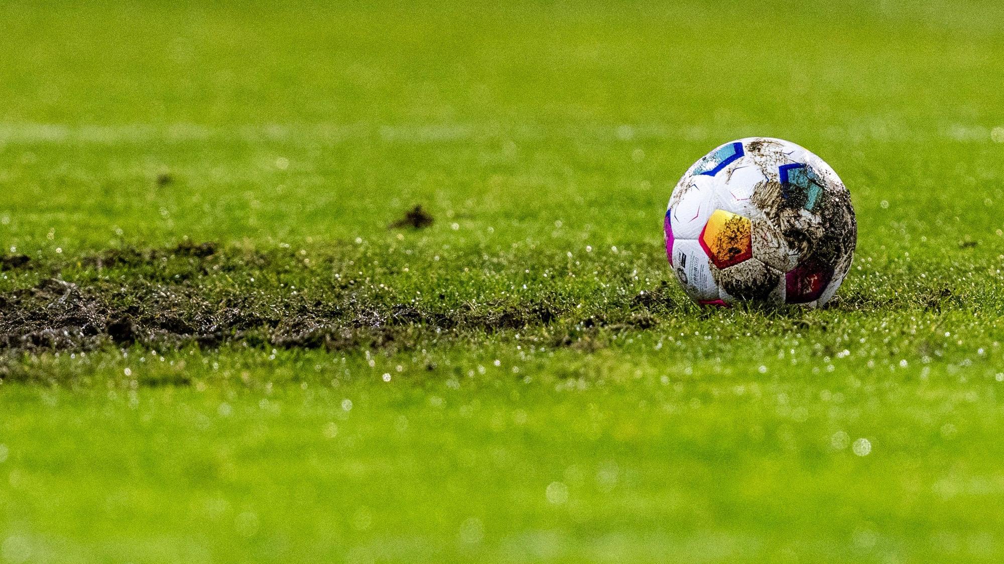 Ein Fußball liegt am Elfmeterpunkt im matschigen Rasen.