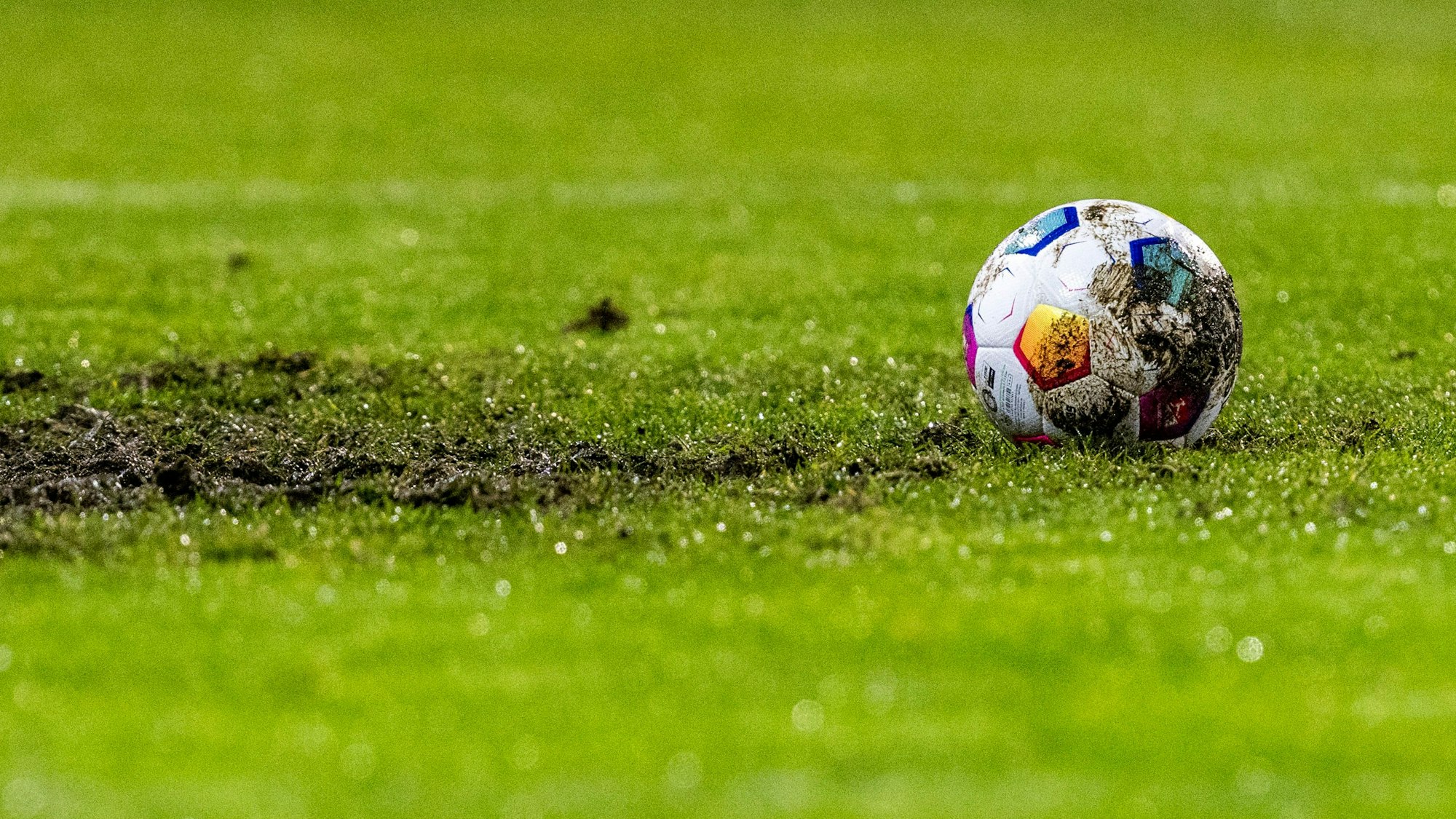 Ein Fußball liegt am Elfmeterpunkt im matschigen Rasen.