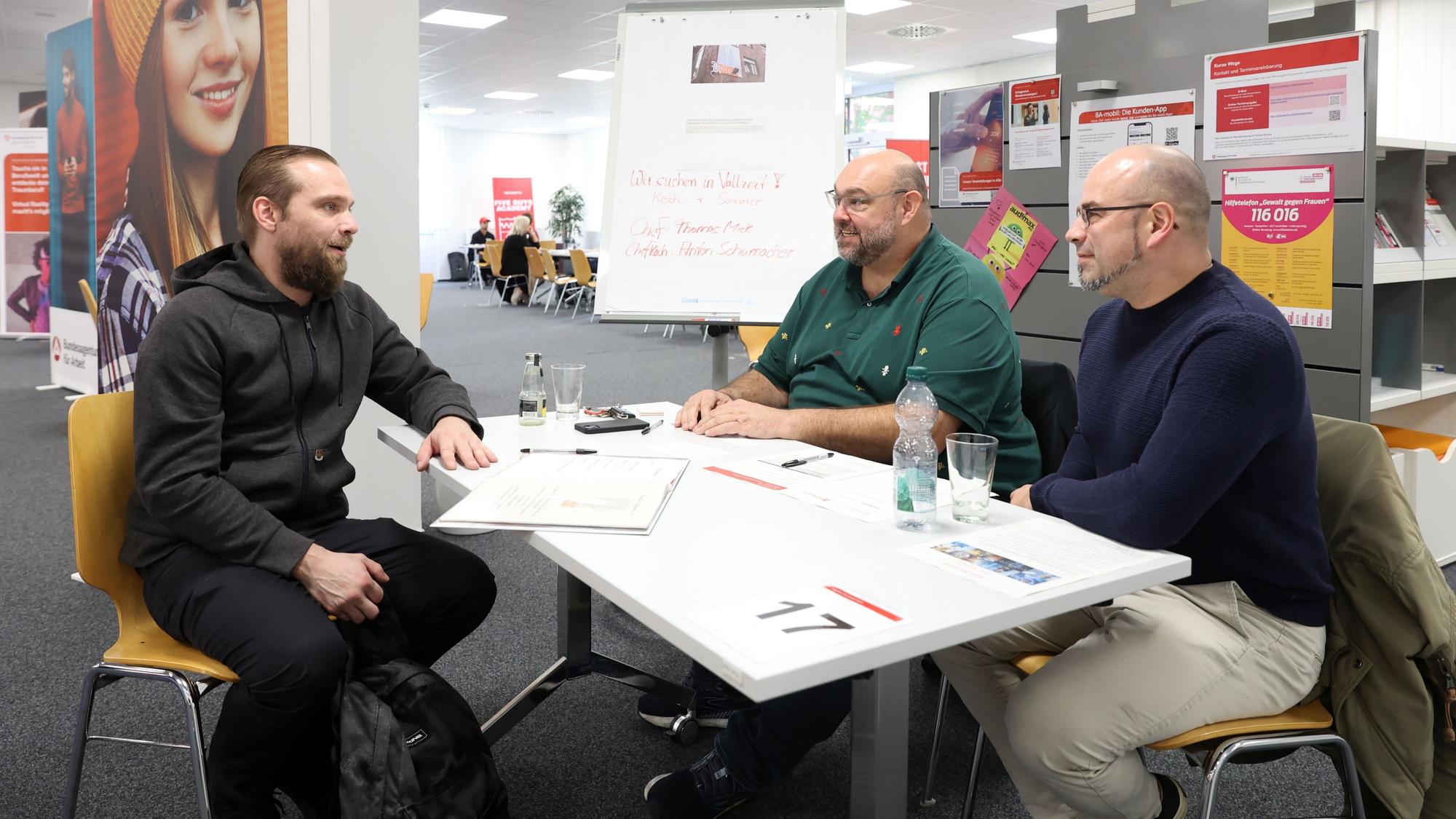Konstantin Boos, Thomas Mick und Anton Schumacher
sitzen an einem Tisch in der Arbeitsagentur Köln