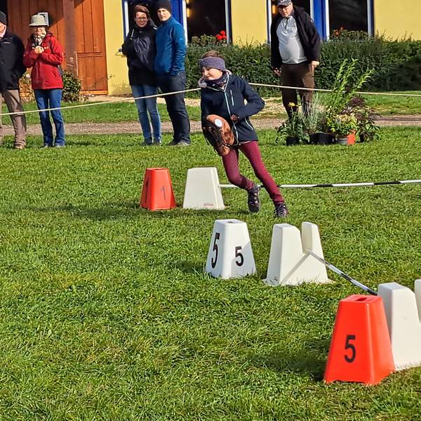 Das Bild zeigt das Mädchen, wie es mit einem Steckenpferd einen Parcours bewältigt.