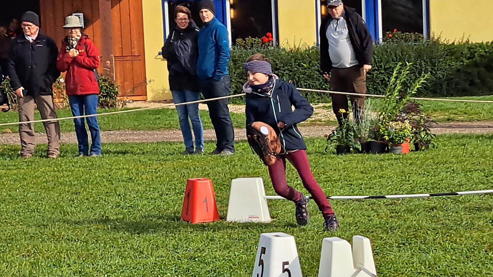 Das Bild zeigt das Mädchen, wie es mit einem Steckenpferd einen Parcours bewältigt.