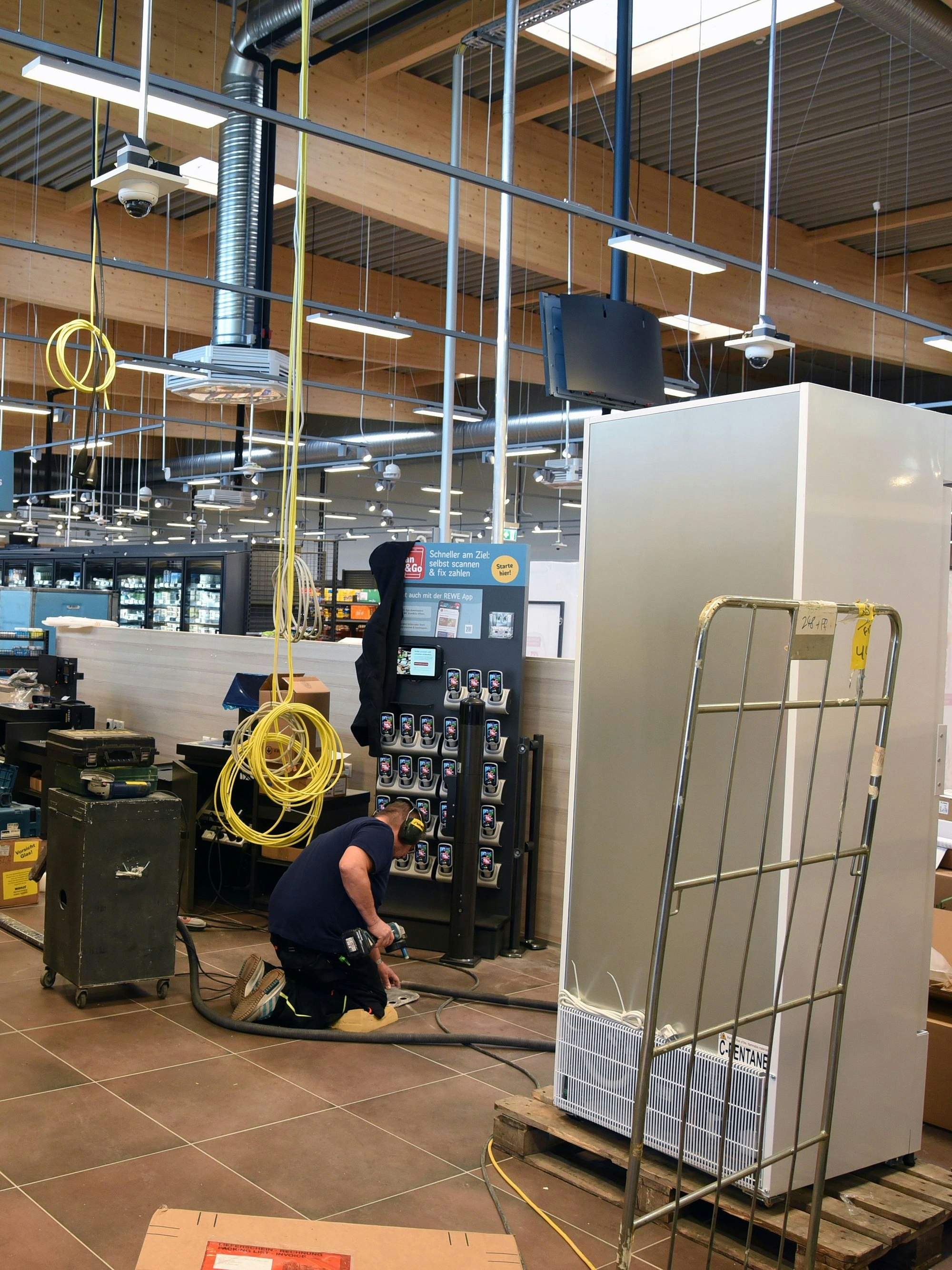 Ein Handwerker kniet auf dem Boden und arbeitet, Kabel hängen aus der Decke, die letzten Arbeiten im neuen Rewe in Engelskirchen-Ründeroth werden erledigt.