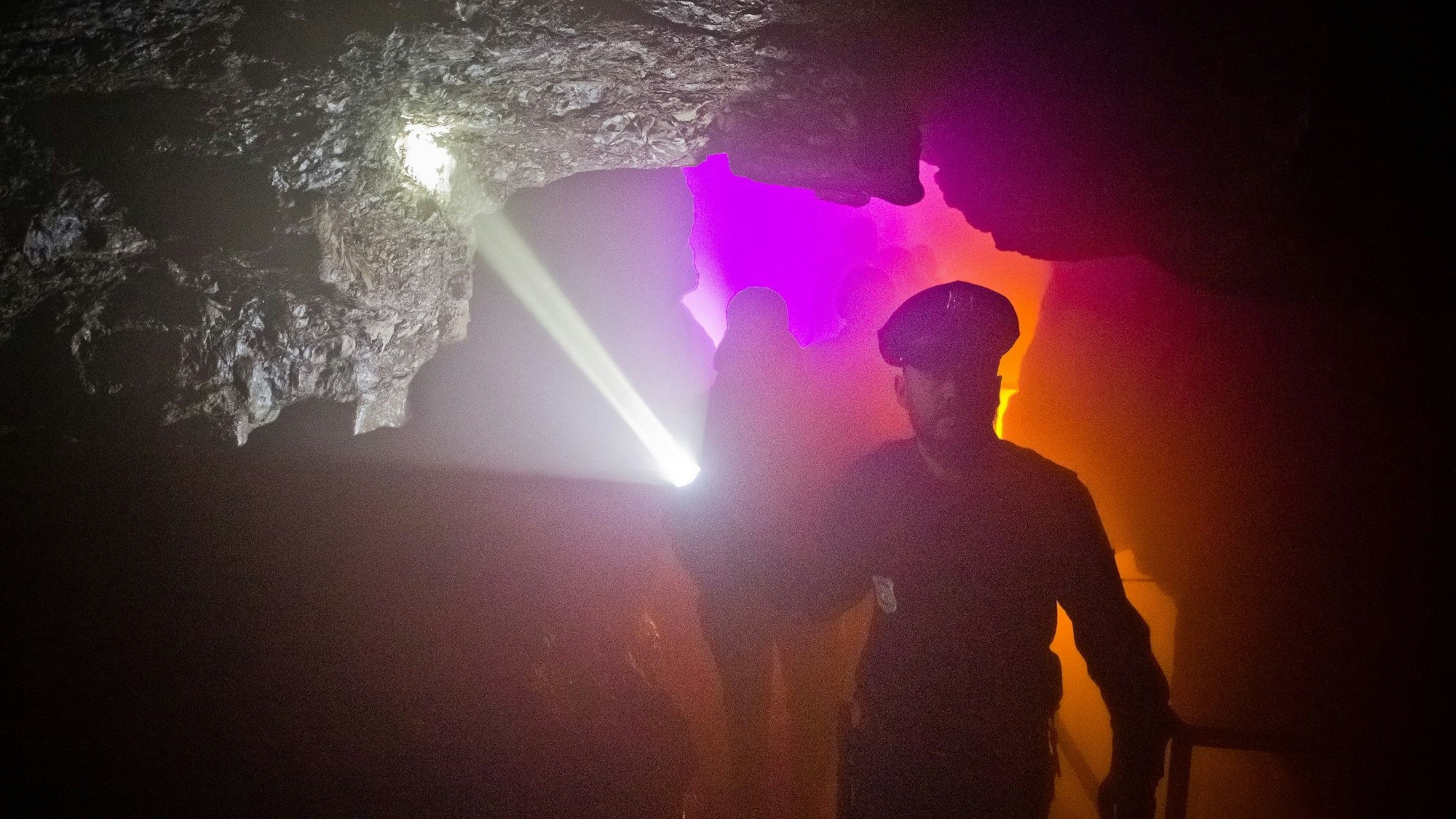 Ein Mann mit einer Taschenlampe führt eine Gruppe Menschen durch eine dunkle Höhle.