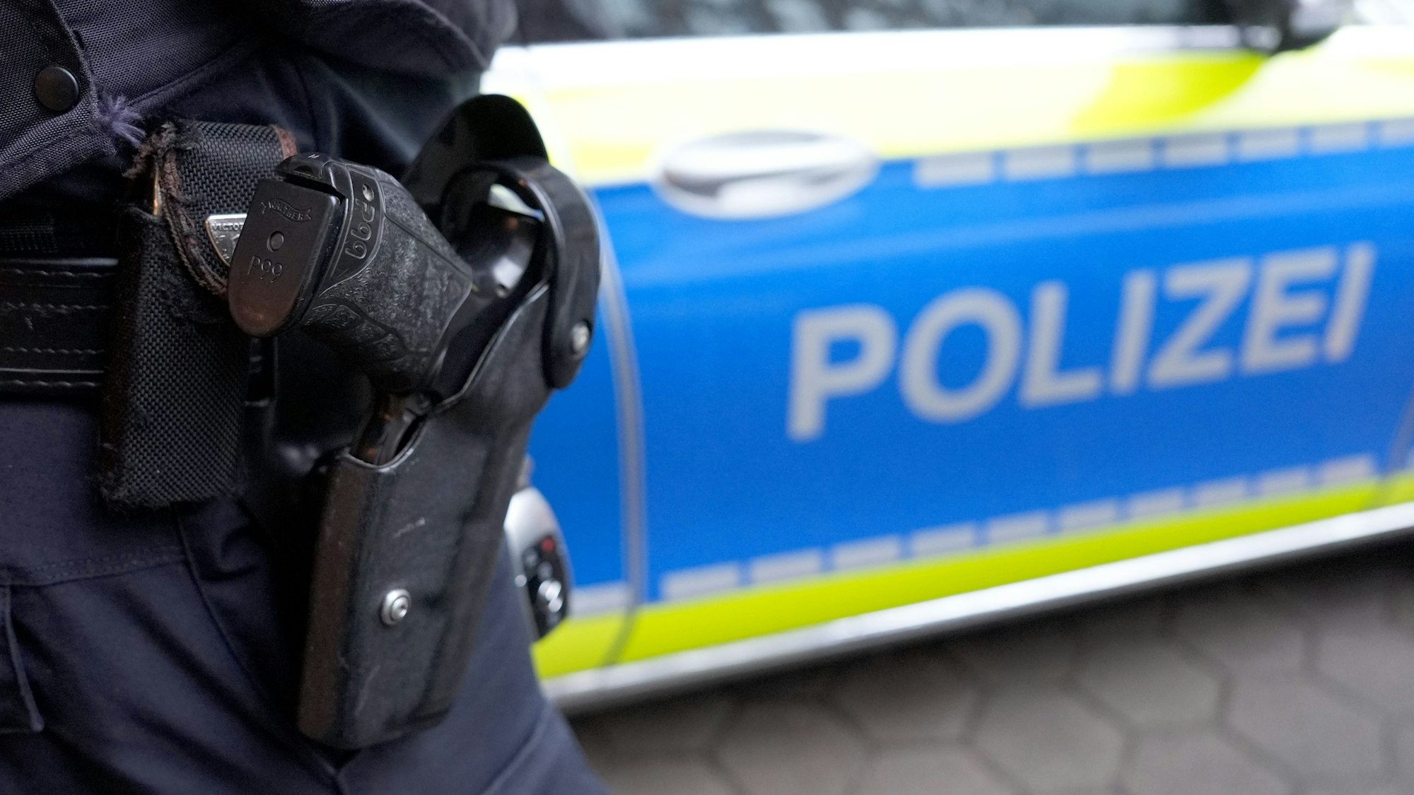 Das Bild zeigt ein Polizeiauto, vor dem ein Polizist steht.
