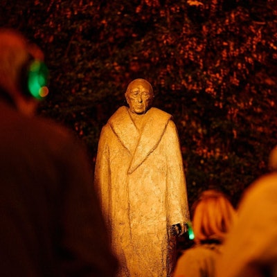 Menschen mit Kopfhören stehen vor einer Statue von Konrad Adenauer.