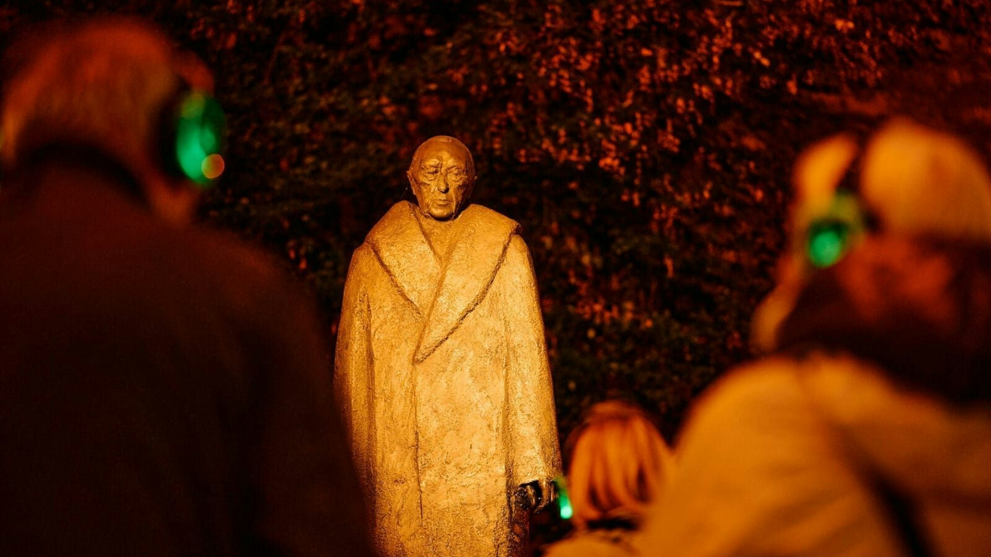 Menschen mit Kopfhören stehen vor einer Statue von Konrad Adenauer.