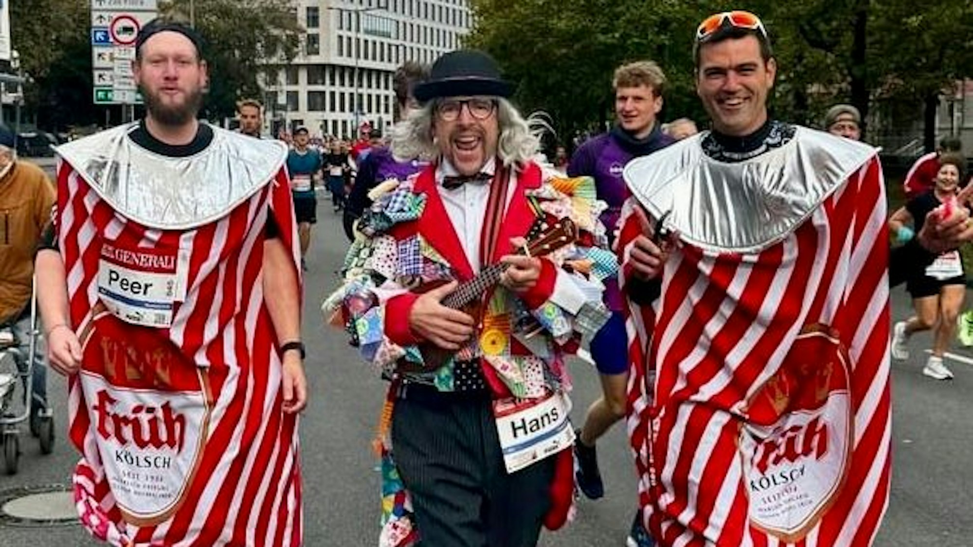 Zwei Männer in Gewändern als Kölschdosen laufen neben dem als Süper verkleideten Löhr.