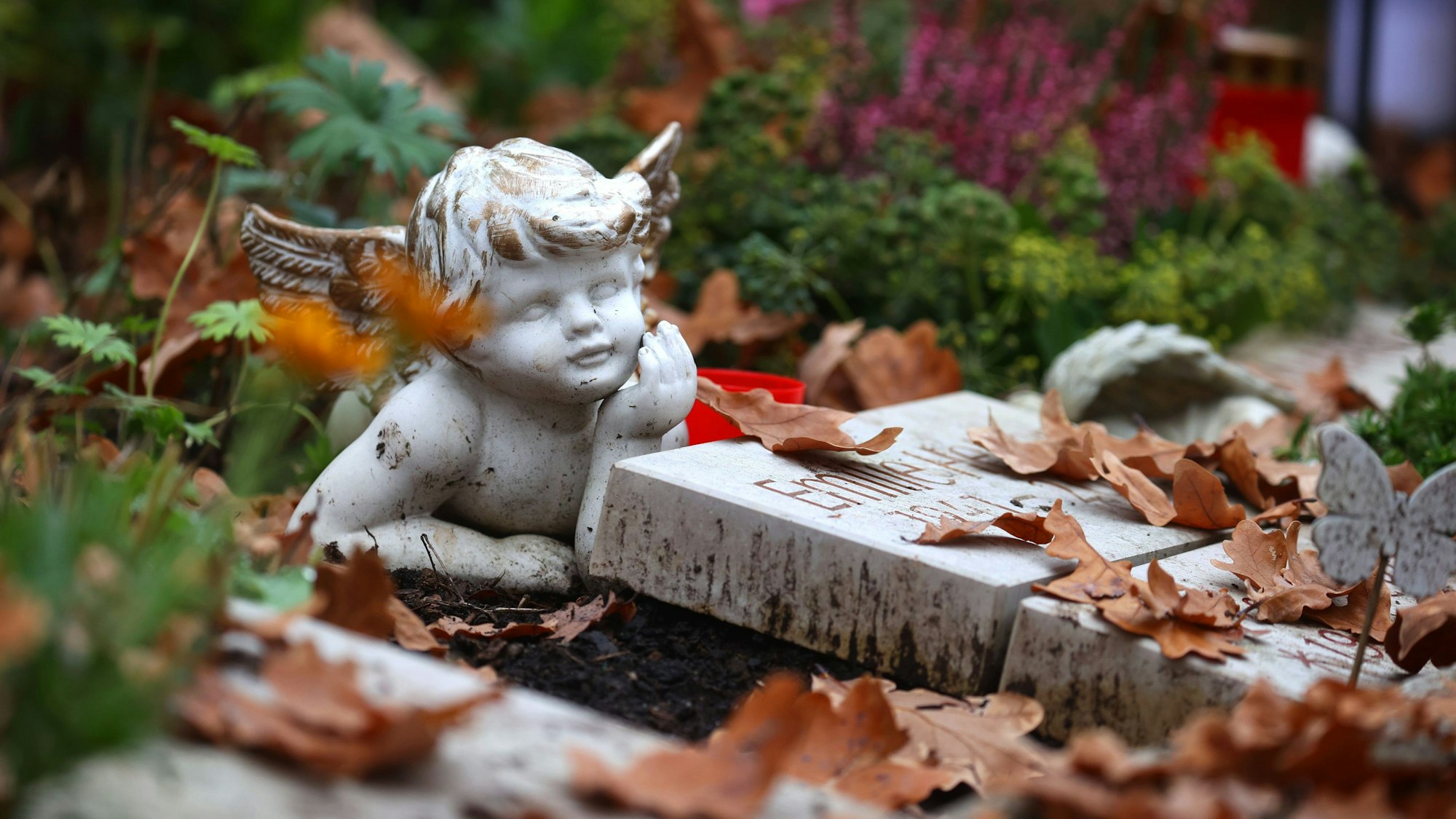 Eine Engelsfigur liegt auf dem Zentralfriedhof auf einem Grab zwischen Herbstlaub.
