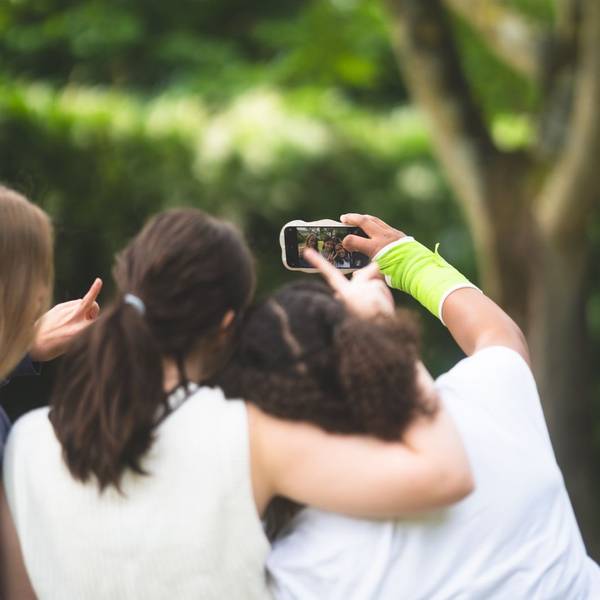 Drei Teenagerinnen sind von hinten zu sehen, sie umarmen sich und machen ein Selfie-Video mit dem Smartphone,