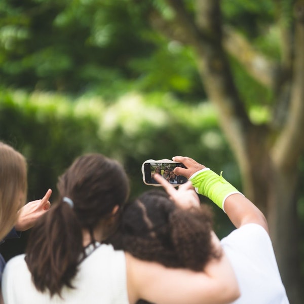 Drei Teenagerinnen sind von hinten zu sehen, sie umarmen sich und machen ein Selfie-Video mit dem Smartphone,