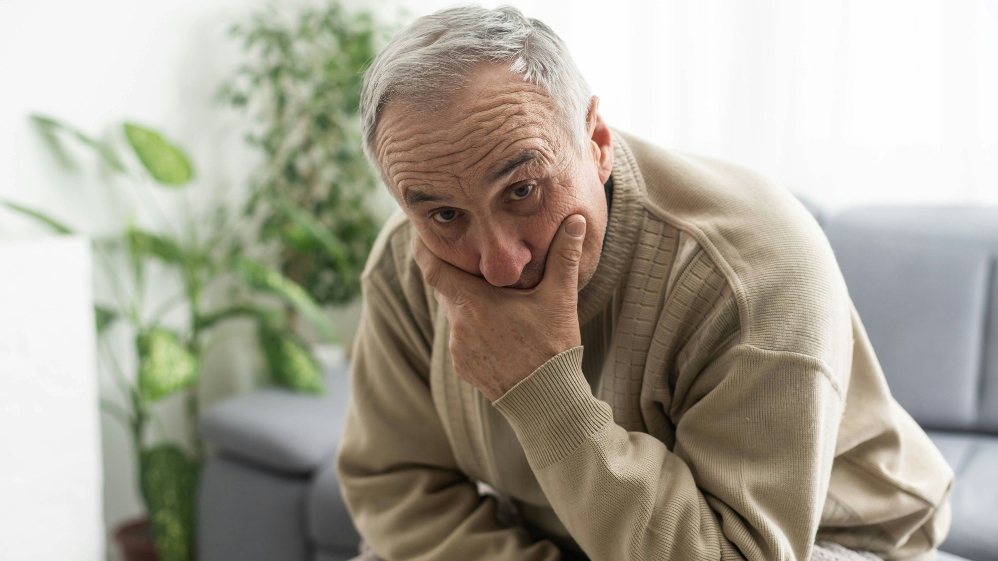 Ein alter Mann denkt nachdenklich auf seinem Sofa.