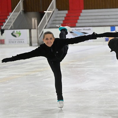 Zwei junge Frauen zeigen ein Kunststück auf Schlittschuhen.