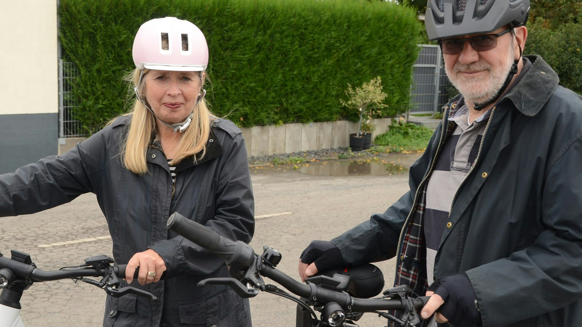 Ein Mann und eine Frau stehen neben ihren Fahrrädern. Beide tragen dunkle Windjacken und einen Fahrradhelm.