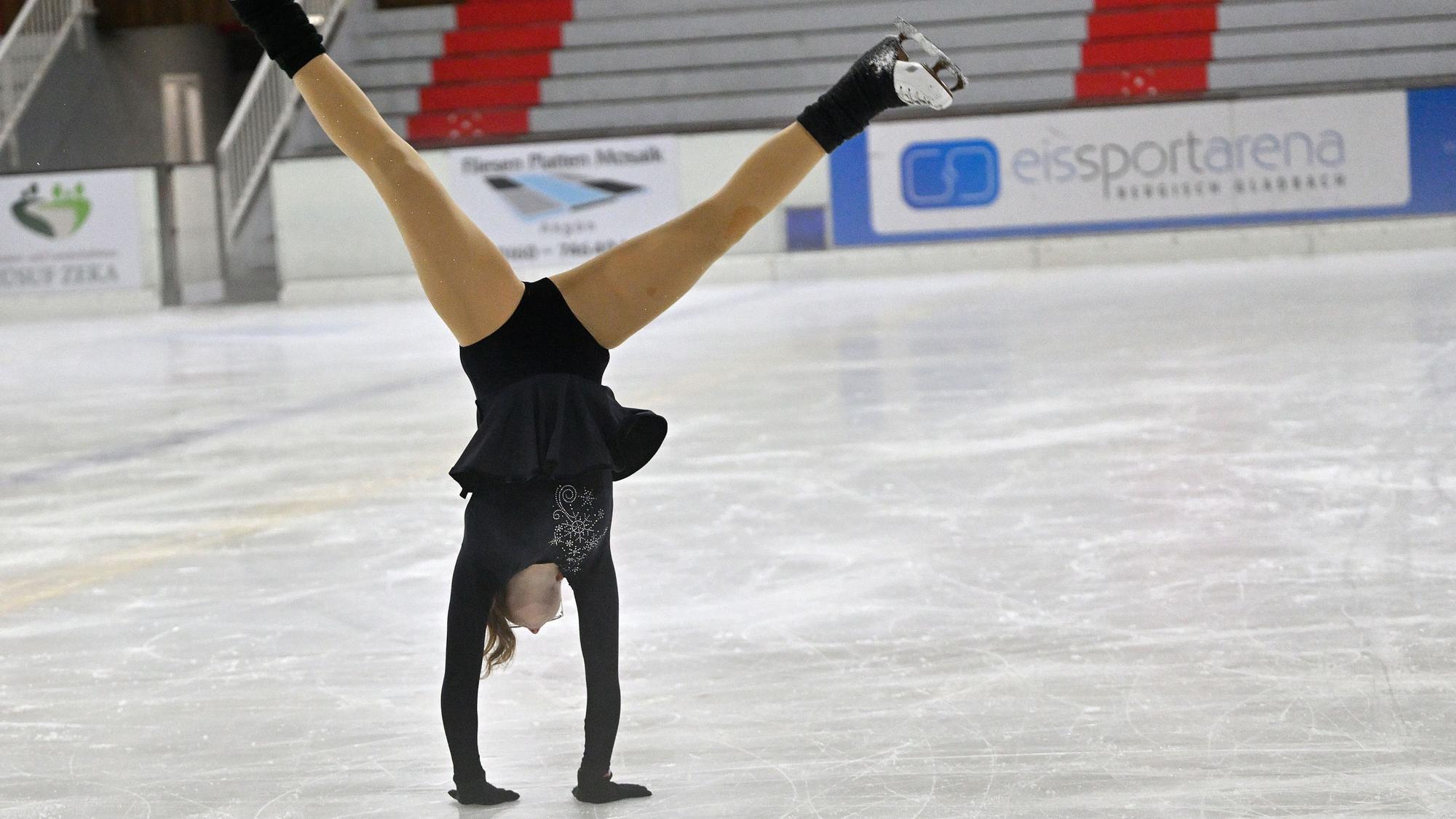 Das Foto zeigt ein Mädchen, das einen Handstand auf dem Eis macht.