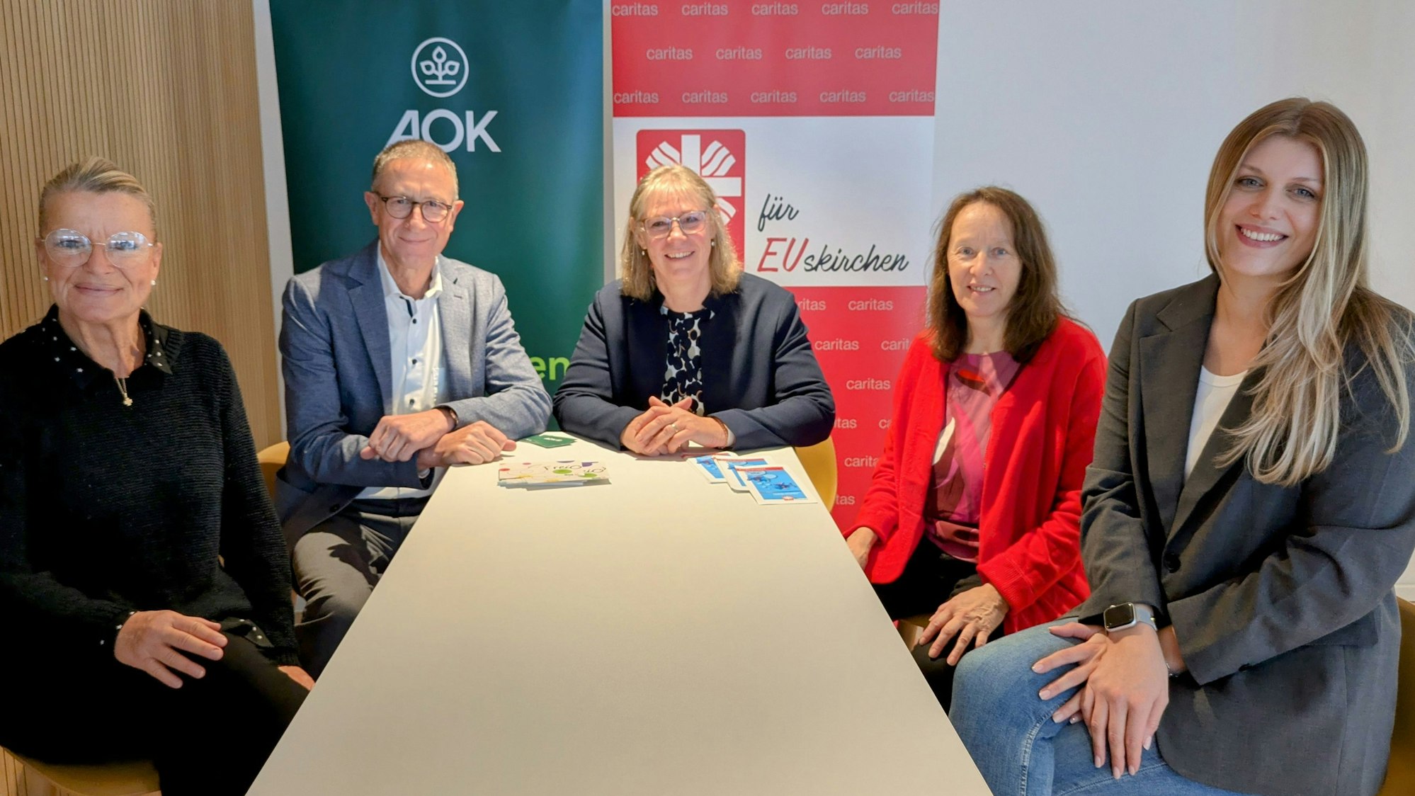 Berit Lamche-Fortouna (AOK), Helmut Schneider (Regionaldirektor AOK Bonn/Rhein-Sieg-Kreis/Euskirchen), Maria Surges-Brilon (Caritas), Dorothee Koch (Diplompädagogin) und Gianna Winkle (Sozialpädagogin) sitzen um einen Tisch.