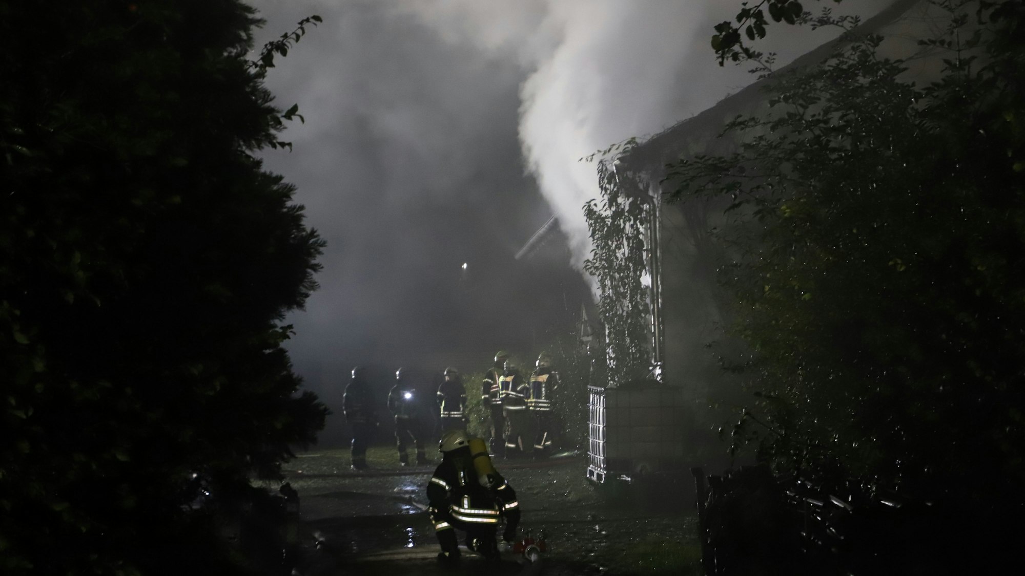 Feuerwehrleute stehen vor einem Haus, aus dem es raucht.