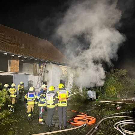 Feuerwehrleute stehen vor einem Gebäude, aus dem es raucht.