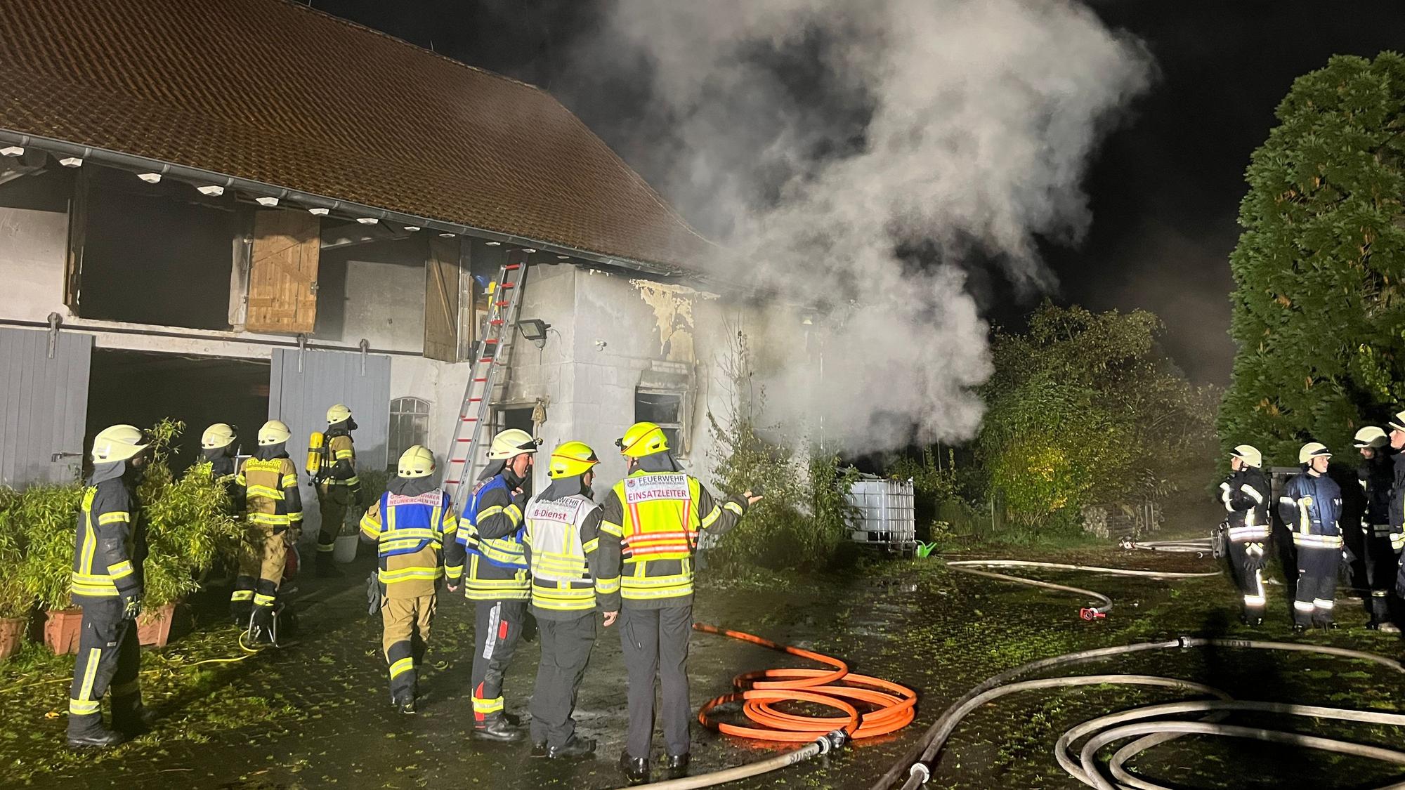 Feuerwehrleute stehen vor einem Gebäude, aus dem es raucht.