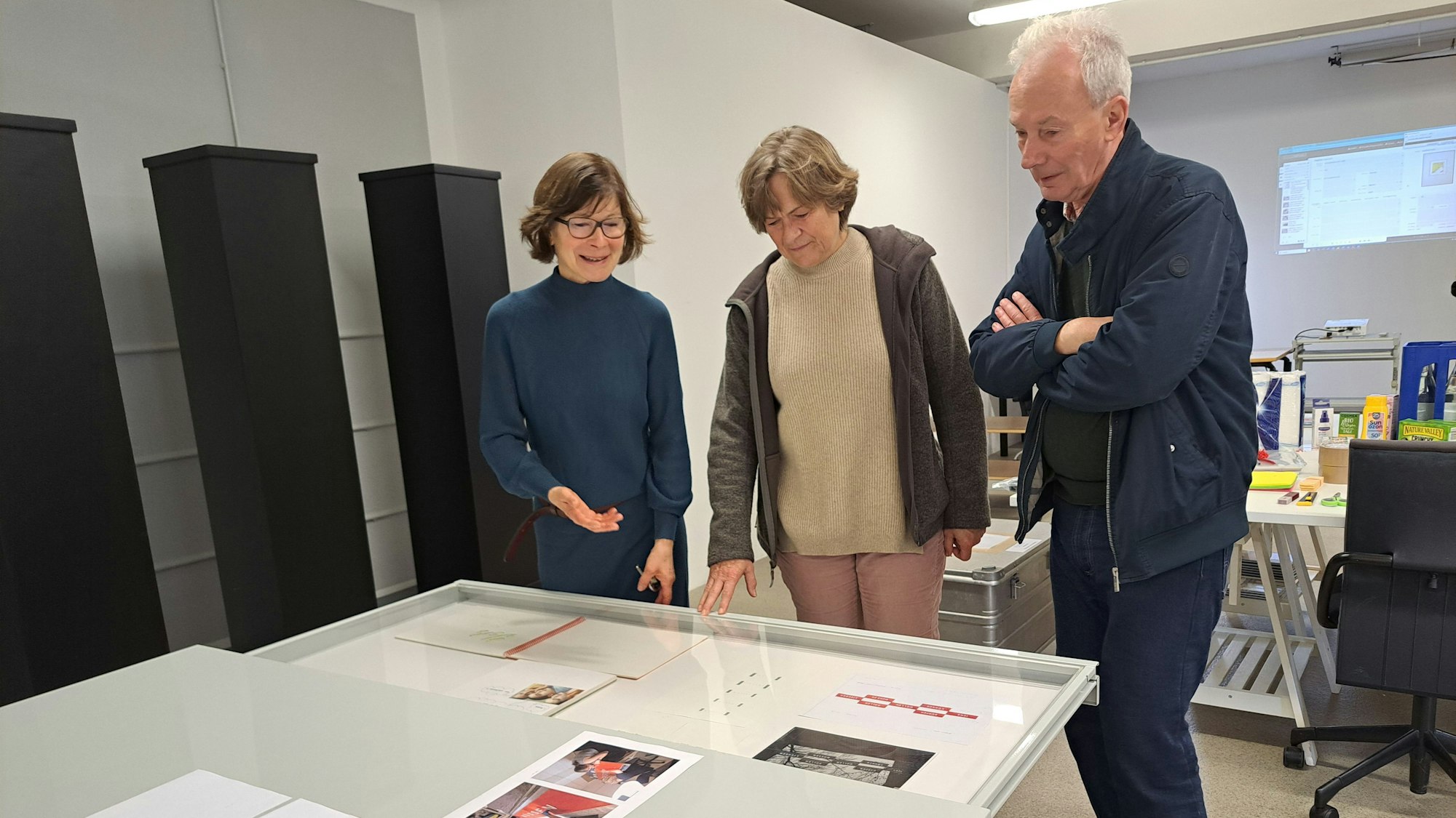 Zwei Frauen und ein Mann schauen sich Kunstwerke, die vor ihnen liegen, an.