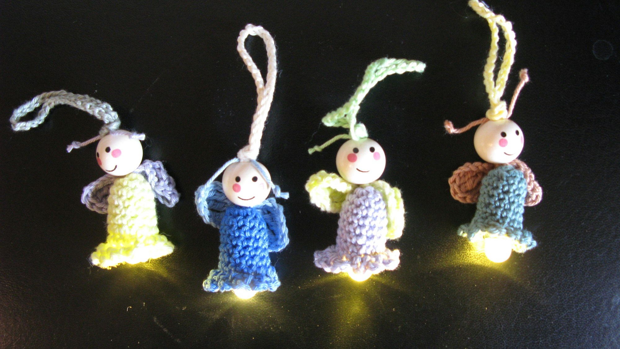 Vier etwa fingergroße, gehäkelte Püppchen mit leuchtenden Lämpchen.