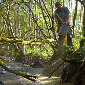 Mithilfe eines Saugbaggers leitet ein Arbeiter Kies in einen Bach.