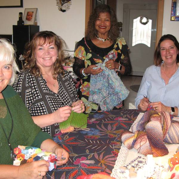 Vier Frauen mit Strickarbeiten in den Händen an einem Tisch.