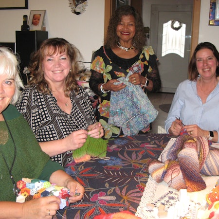 Vier Frauen mit Strickarbeiten in den Händen an einem Tisch.