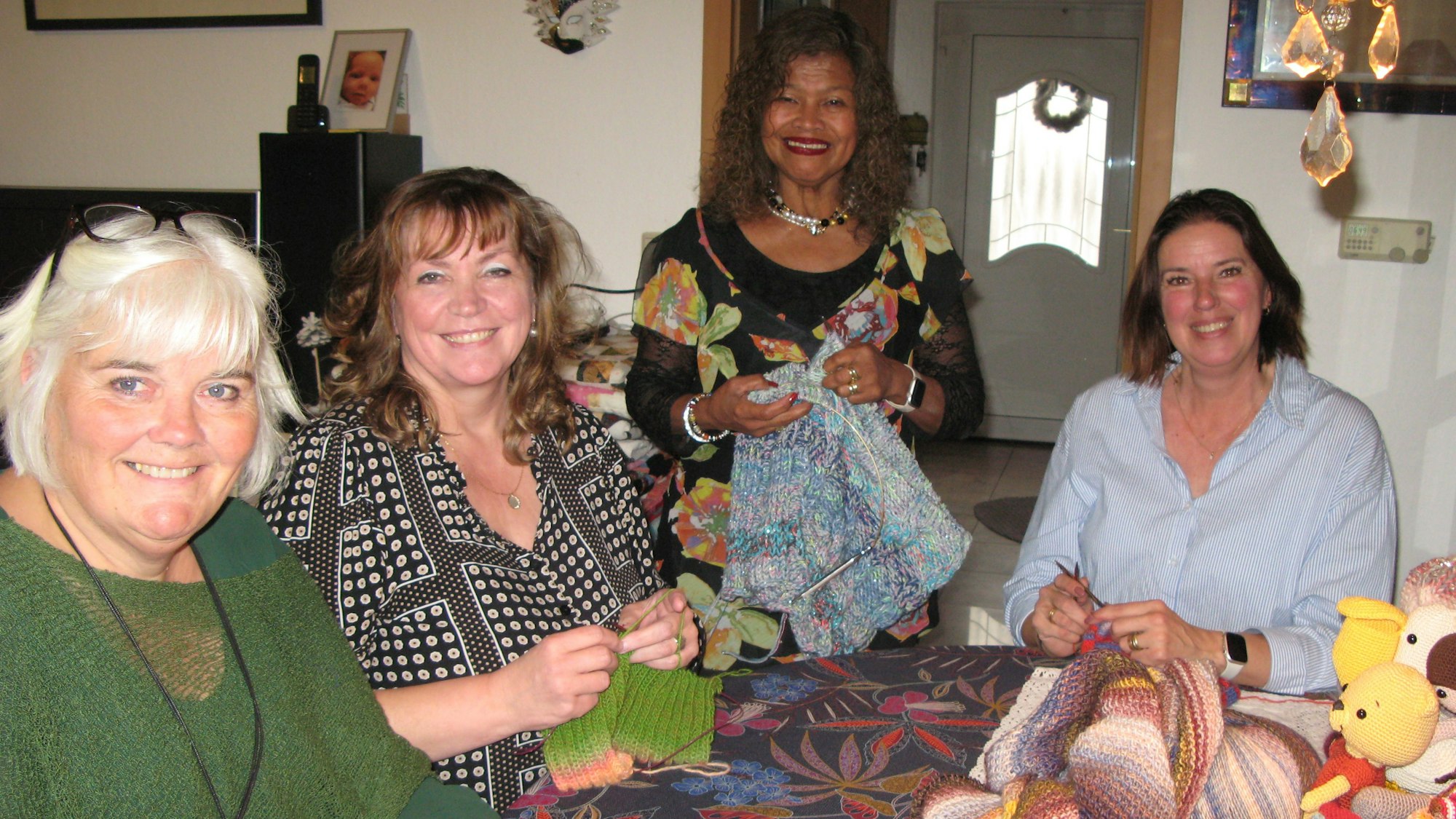 Vier Frauen mit Strickarbeiten in den Händen an einem Tisch.