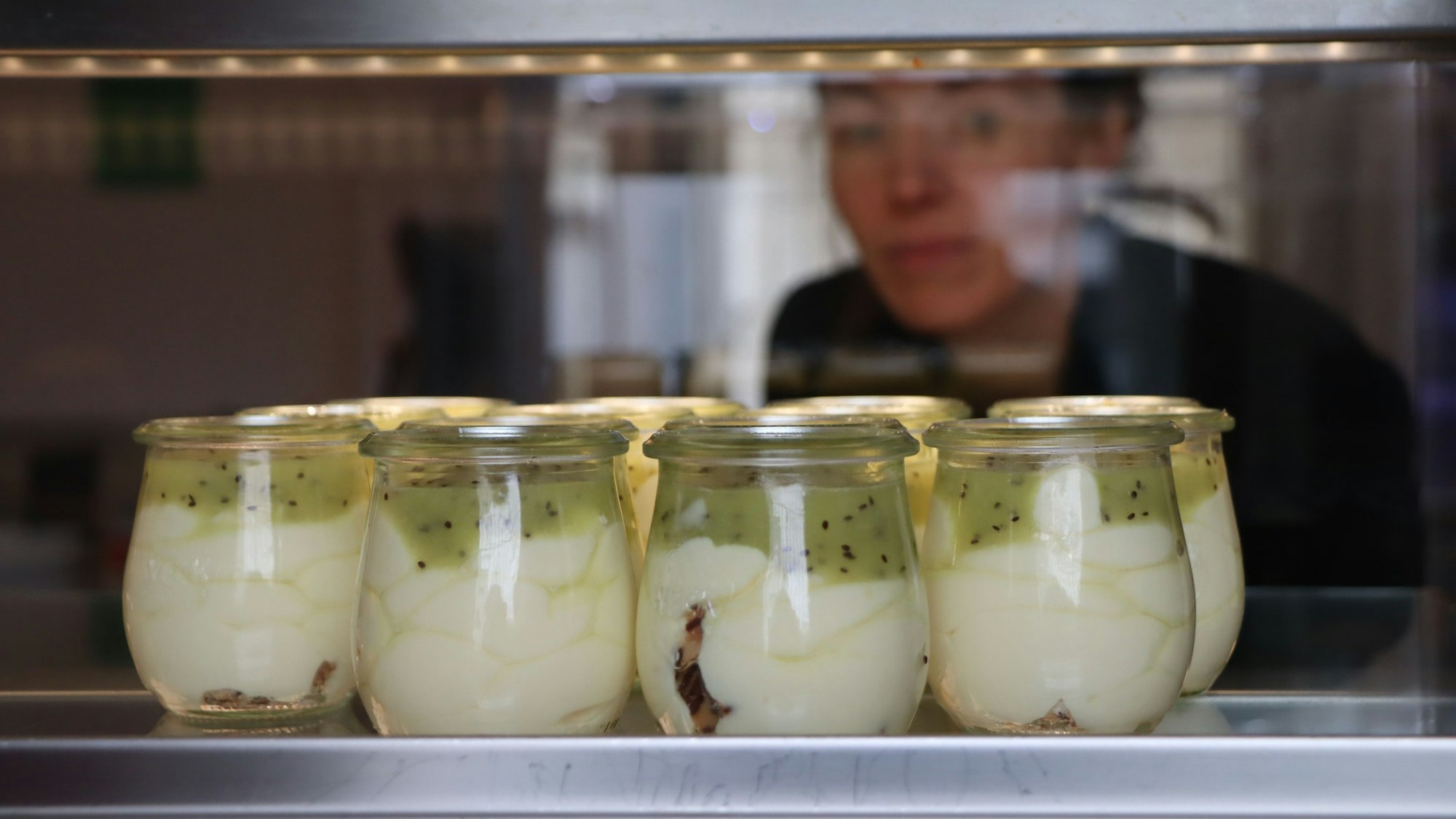 Gläschen stehe hinter einer Scheibe, eine Frau schaut durch die Scheibe.