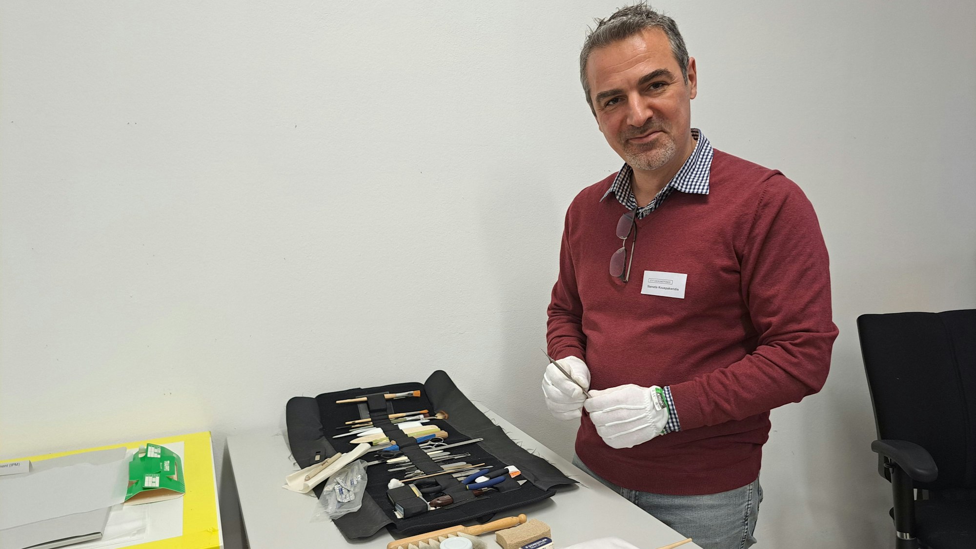 Ein Mann hat viele Werkzeuge vor sich liegen, er trägt bei seiner Handschuhe.