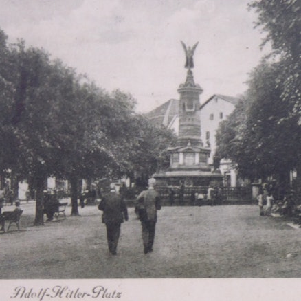 Eine alte Schwarzweiß-Aufnahme des Siegburger Marktplatzes mit Menschen und der Säule mit der Siegesgöttin.